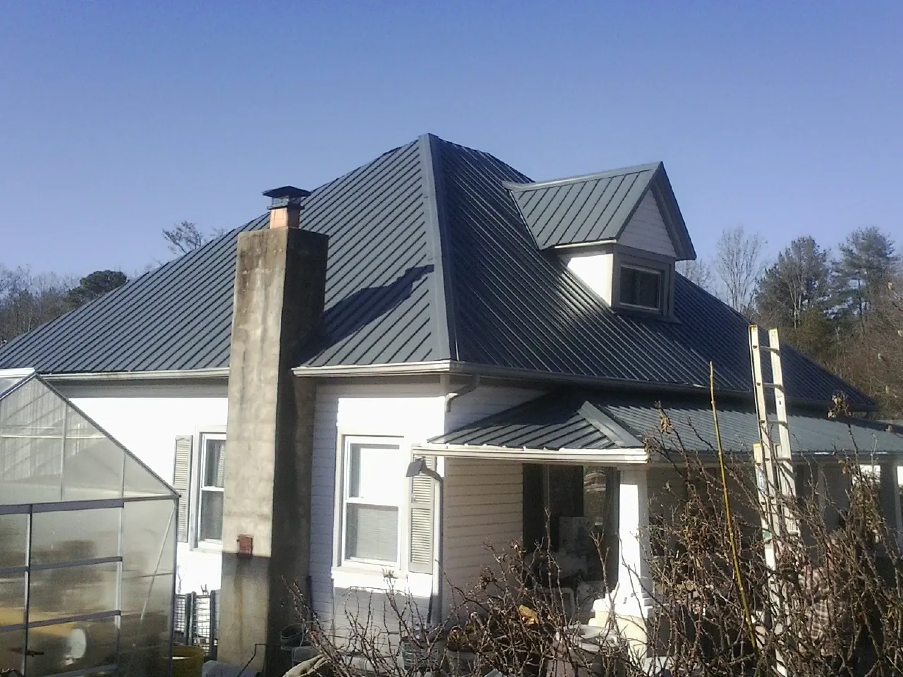 Dark blue standing seam metal roof on a white farmhouse with dormer — Slate & Tile Roof Repair by Roofing Brothers in Herkimer