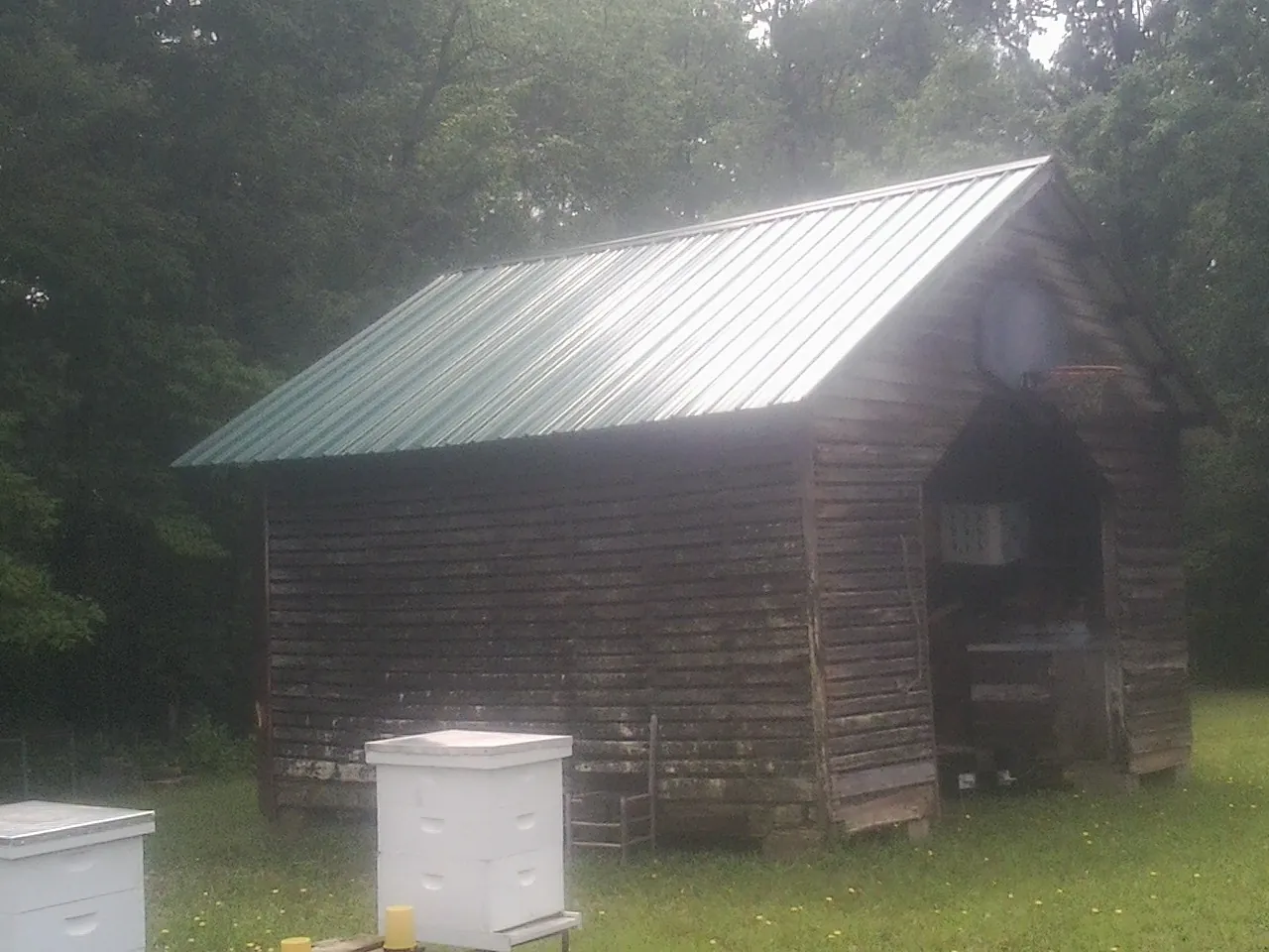 Green metal roof on a weathered barn beside stacked beehives in Herkimer
