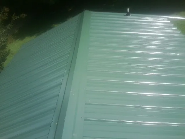 New green metal panels meeting at the ridge of a roof — Flat Roof Repair work by our crew in Herkimer