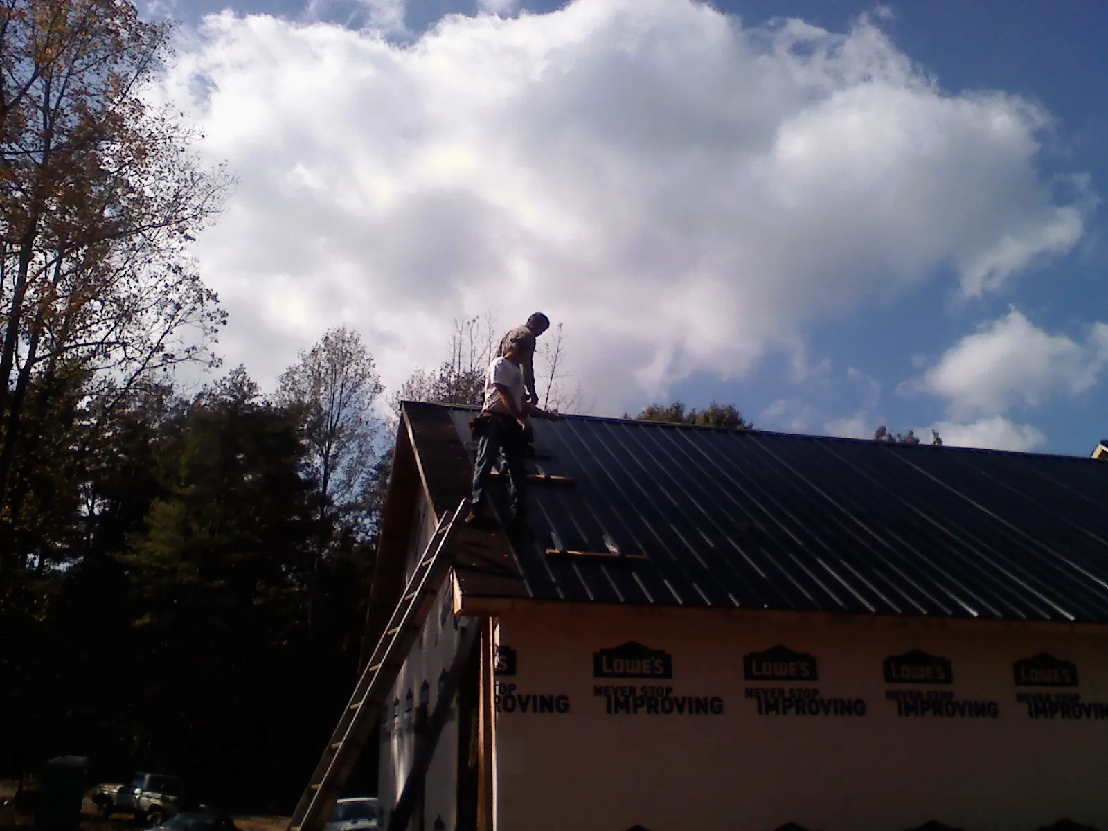 Roofer fastening dark metal panels high against a cloudy sky, from a Roof Inspection job in Herkimer
