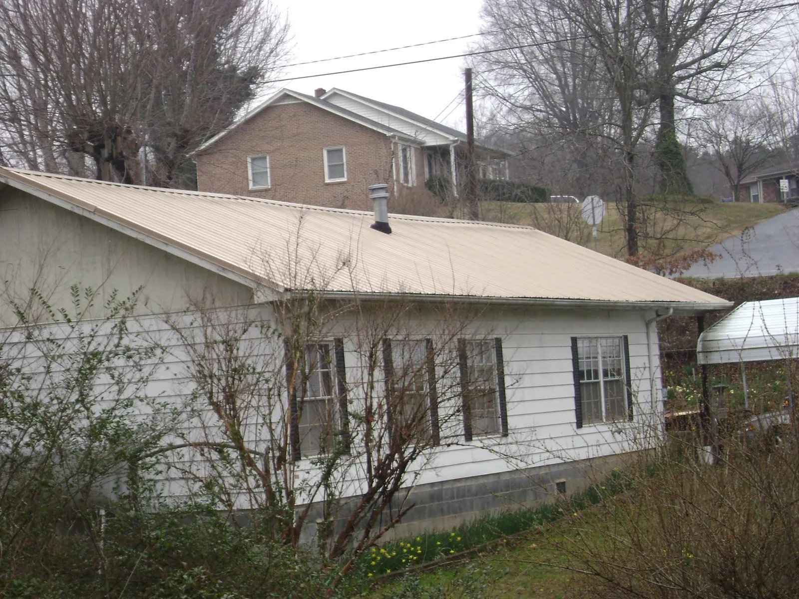 Tan metal roof on a white sided house set into a hillside — Commercial Roofing by Roofing Brothers in Herkimer