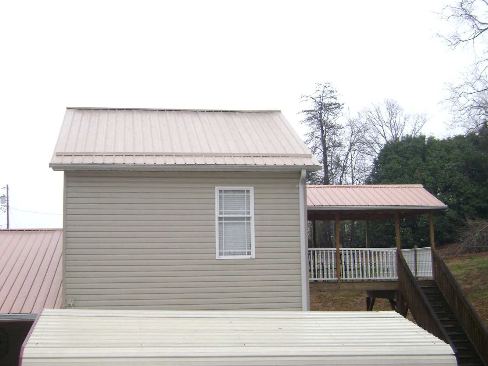 Tan metal roofs on a two story addition and attached porch, from a Roof Replacement job in Herkimer